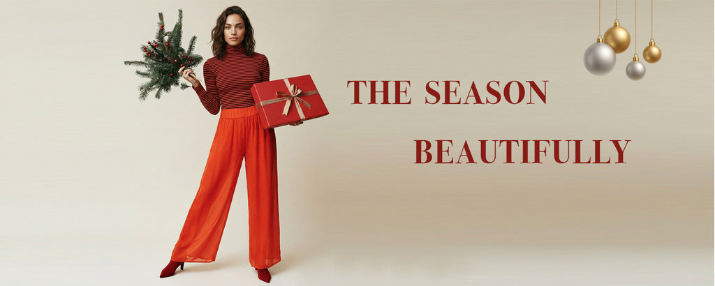 Woman in red top and orange pants holding a gift with Christmas decorations on a beige background.