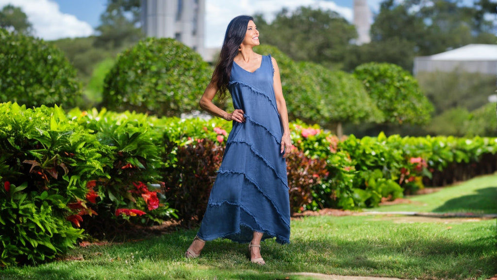 Woman in a blue dress standing in a garden with greenery and flowers.