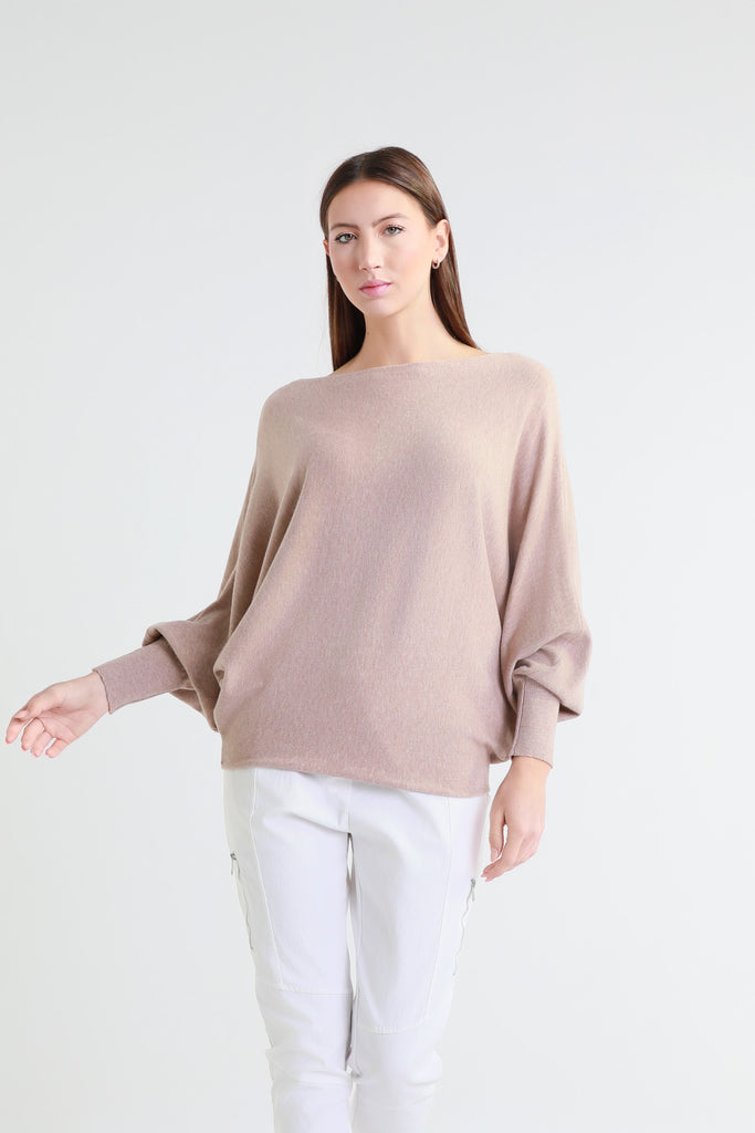 Woman wearing a beige sweater and white pants on a white background