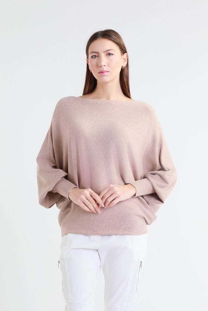Woman wearing a beige sweater and white pants on a light gray background