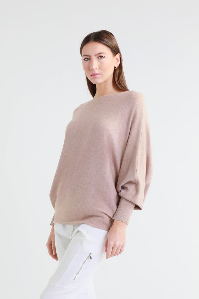 Woman wearing a beige sweater and white pants on a white background
