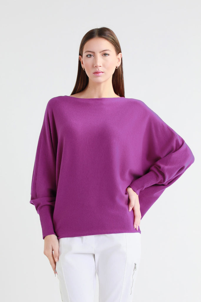 Woman wearing a purple sweater and white pants on a light gray background