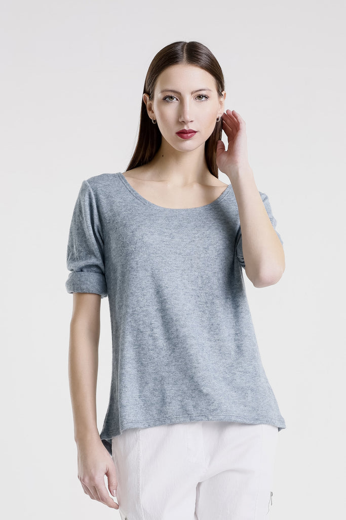 Woman wearing a gray top and white pants against a plain background