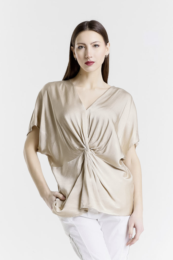 Woman wearing a beige top with a knot detail on a white background