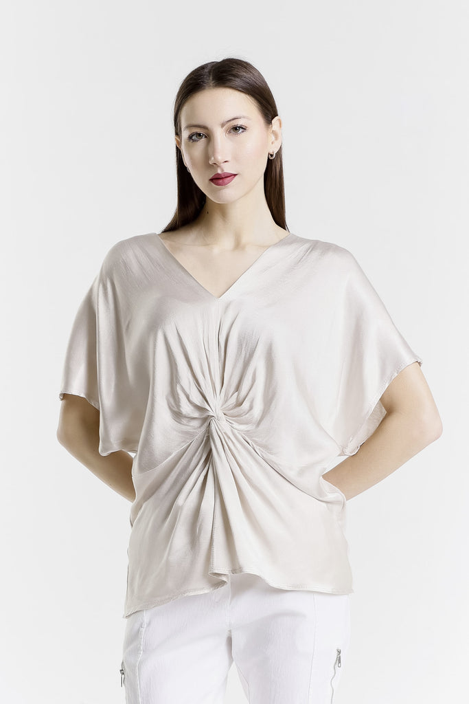 Woman wearing a beige top with a knot detail on a white background