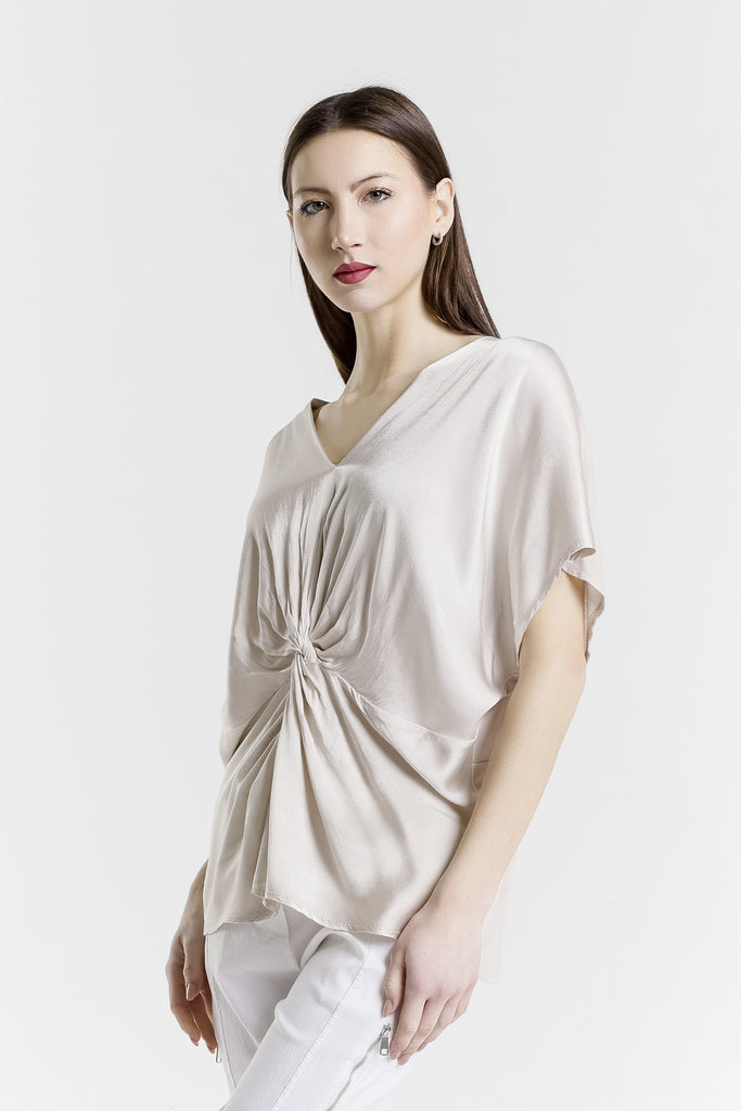 Woman wearing a beige top with a knot detail on a white background