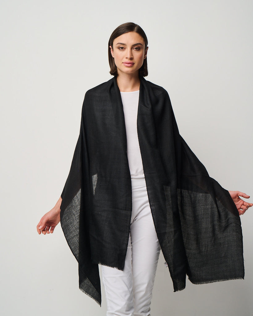 Woman wearing a black shawl over a white outfit on a plain background
